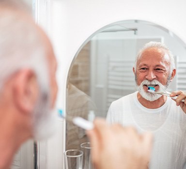 Man smiling while brushing his teeth in bathroom