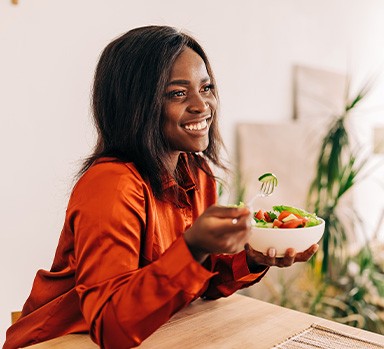 Woman smiling while eating healthy snack at home